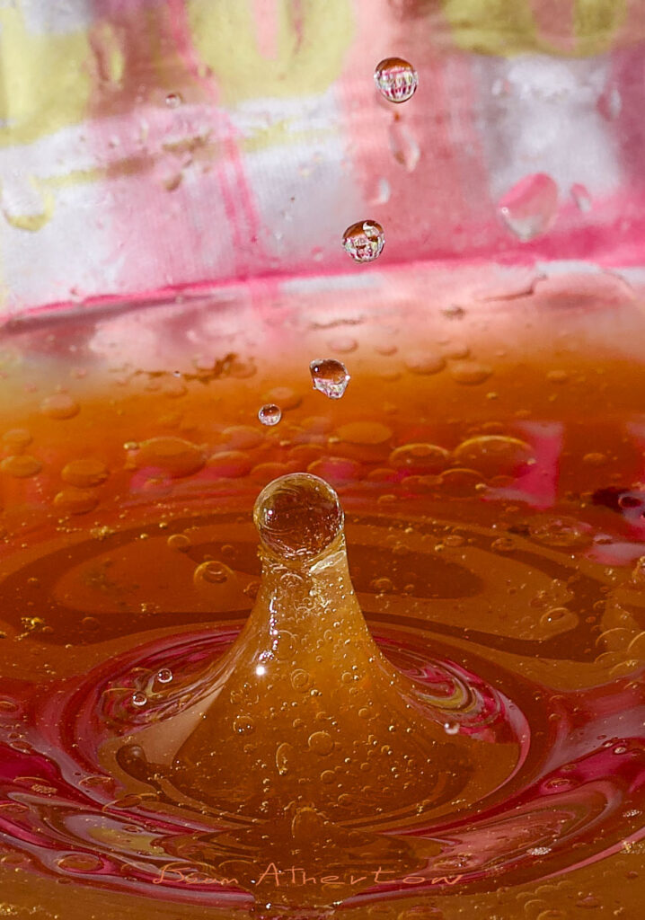 One big water drop with 5 trailing water droplets with reflections of background in the droplets